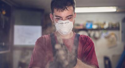 A young man wearing a mask to avoid dust while working in the garage