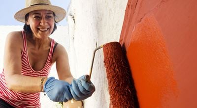 Smiling woman painting wall with red paint outdoors